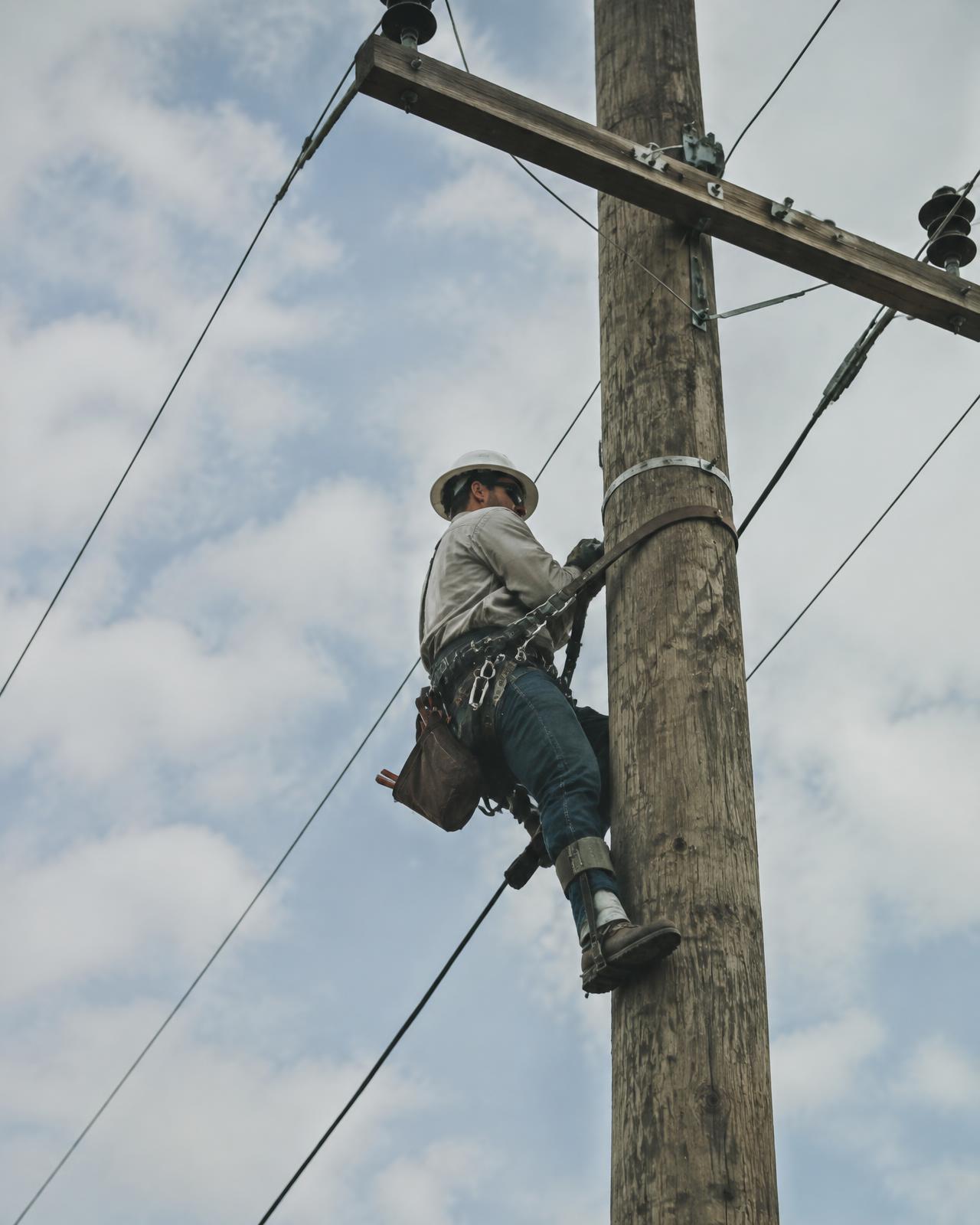 Lineman working high on a utility pole beneath an open sky